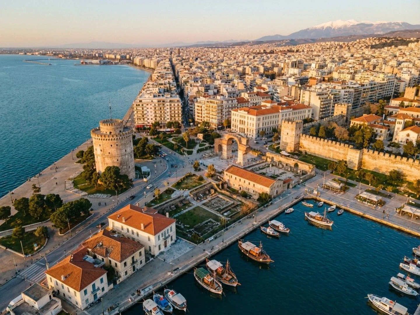 Aerial view of Thessaloniki's White Tower on Thermaic Gulf with Byzantine walls, harbor boats, and Mount Olympus backdrop